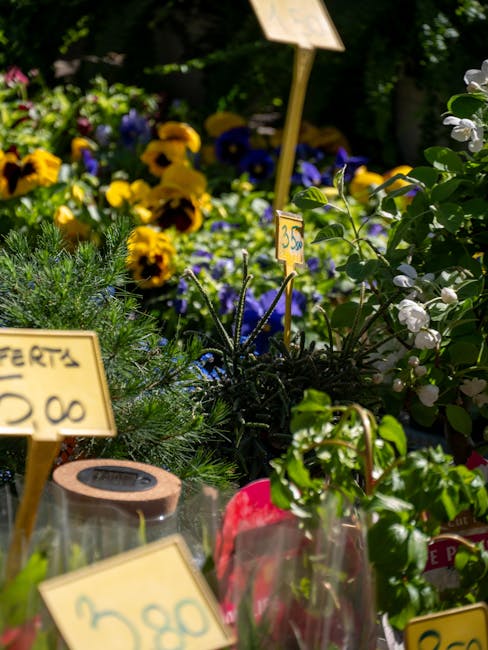 A vibrant display of fresh flowers arranged outdoors with a variety of species including yellow pansies, purple violets, white blossoms, and green foliage. The flowers are densely packed and presented